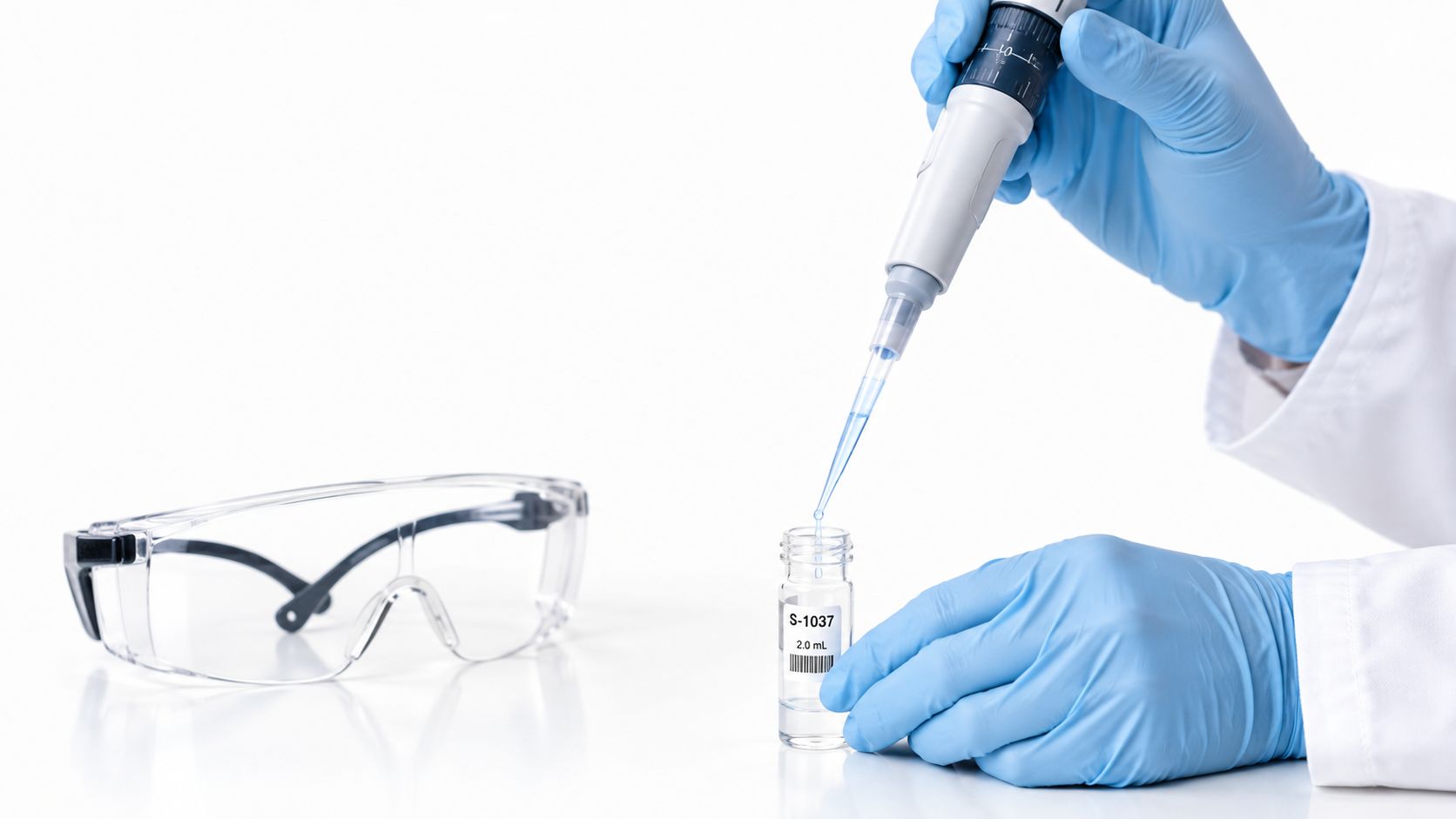 A laboratory scientist wearing blue gloves uses a micropipette to dispense liquid into a small glass vial.