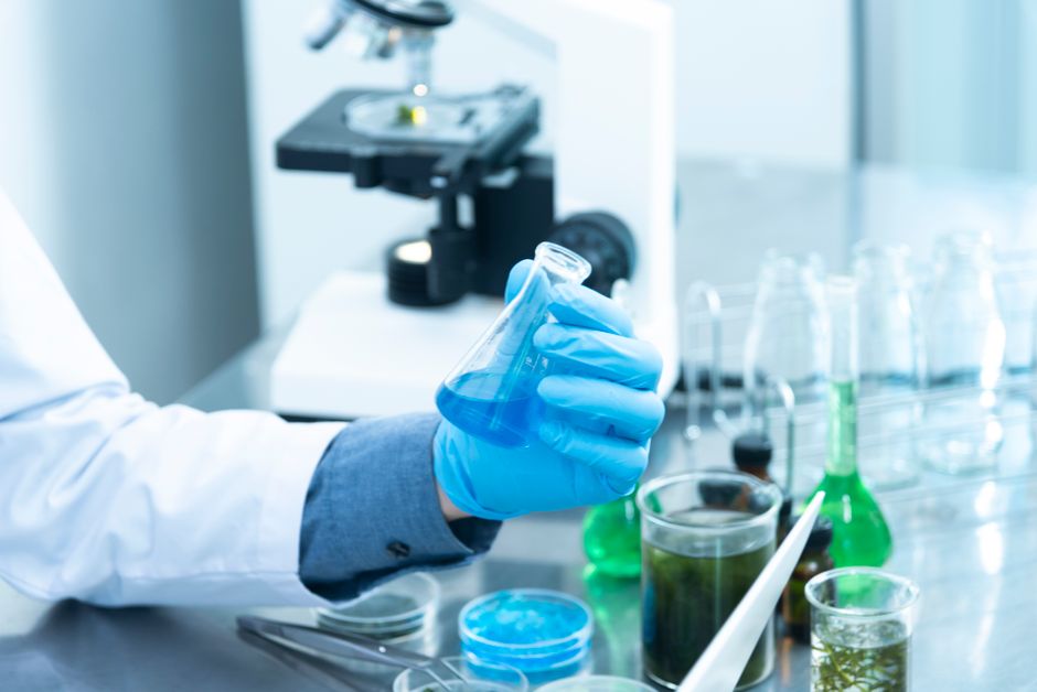 Understanding Reconstitution Solutions. Scientist in gloves analyzing blue liquid in a laboratory setting with microscope and glassware.